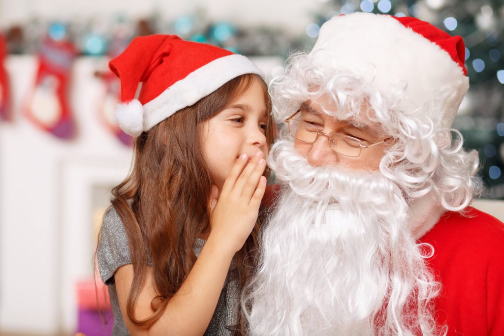 Let my dreams come true. Nice little girl holding her hand near face and talking with Santa while waiting for holiday